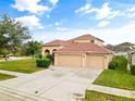 Beige two-story home featuring a three-car garage, tile roof, arched entry, and a well-manicured lawn at 2604 Dakota Rock Dr, Ruskin, FL 33570