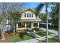 Inviting yellow two-story home featuring a cozy front porch, mature landscaping and long driveway on a sunny day at 445 13Th Ne Ave, St Petersburg, FL 33701
