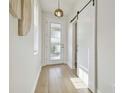 Bright hallway featuring wood floors, natural light, a decorative sliding barn door, and modern light fixtures at 17628 Breakaway St, Land O Lakes, FL 34638