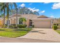 Single-story home featuring a well-manicured lawn, lush landscaping, and a paver driveway to an attached garage at 2218 Mayfield Palms Ln # 323, Sun City Center, FL 33573