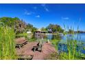 Scenic view of a lake with a private dock and seating, surrounded by lush greenery and blue skies at 3046 Lake Padgett Dr, Land O Lakes, FL 34639