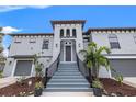 Inviting entrance of a two-story home featuring a stairway leading to the front door and lush tropical landscaping at 58 Inness Dr, Tarpon Springs, FL 34689