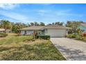 Well-maintained single-story home with lush lawn, mature trees, and spacious two-car garage under a blue sky at 37157 Foxrun Pl, Zephyrhills, FL 33542