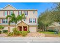 Exterior view of a three story townhome with a red door, one car garage, and landscaped front yard at 876 Callista Cay Loop, Tarpon Springs, FL 34689