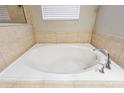 A close-up view of a large, tiled bathtub featuring chrome hardware and a window with blinds at 2111 Roanoke Springs Dr, Ruskin, FL 33570