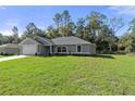 Single-story home with gray siding, a spacious yard, and mature trees surrounding the property at 12040 Pine Warbler Ave, Brooksville, FL 34614