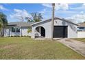 Charming home featuring a stucco exterior, front lawn, palm trees, and an attached garage with a black door at 7431 Abington Ave, New Port Richey, FL 34655