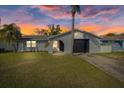 Charming home featuring a stucco exterior, front lawn, palm trees, and an attached garage with a black door at 7431 Abington Ave, New Port Richey, FL 34655