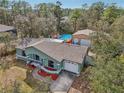 Aerial view of a one-story light-green house with a large pool, detached garage, and mature trees at 13083 Jaywalk Rd, Brooksville, FL 34614