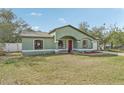 Exterior shot of a light green single-story house with a red door, lawn, and attached garage at 13083 Jaywalk Rd, Brooksville, FL 34614