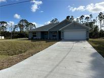 Newly constructed home with a gray exterior, white garage door, and a long concrete driveway at 8005 Tropicaire Blvd, North Port, FL 34291