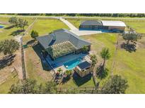 An aerial view showcases a home with a pool, tiki hut and expansive fenced yard, a barn, and a private drive at 25205 67Th E Ave, Myakka City, FL 34251