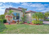 Tan house with brown roof, lush landscaping, and a paved driveway at 20717 Benissimo Dr, Venice, FL 34293