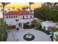 Stunning waterfront estate featuring a terracotta roof, circular driveway with fountain, and lush tropical landscaping at sunset at 4311 Bay Shore Rd, Sarasota, FL 34234
