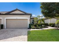 Tan three-car garage villa with paved driveway, landscaping, and walkway at 8199 Varenna Dr, Sarasota, FL 34231