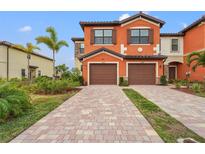 Two-story townhome with orange exterior, two-car garage, and landscaped yard at 20447 Lagente Cir, Venice, FL 34293