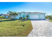 Light blue house with white garage doors, landscaping, and paved driveway at 144 Tournament Rd, Rotonda West, FL 33947