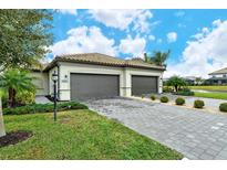 Two-car garage, paver driveway, and landscaped lawn with lush greenery at 15910 Clear Skies Pl, Bradenton, FL 34211