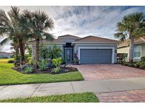 Single-story home with gray garage door, brick paver driveway, and lush landscaping at 19451 Quisto St, Venice, FL 34293