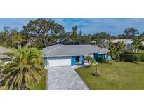 Charming blue home featuring a paved driveway, well-manicured lawn, lush tropical landscaping, and a gray tile roof at 429 N Rossetti Dr, Nokomis, FL 34275