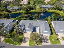 Beautiful aerial view of a single-story home on a pond with fountain, mature trees, and brick driveway at 1666 Pintail Way # 9, Sarasota, FL 34231