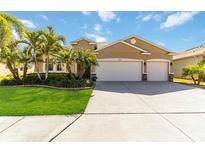 Tan three-car garage house with palm trees and landscaped lawn at 14822 Trinity Fall Way, Bradenton, FL 34212