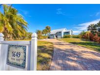 Light blue house with metal roof, paver driveway, and tropical landscaping at 1649 Manor Rd, Englewood, FL 34223