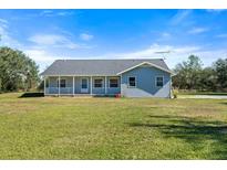 Ranch style home with gray siding, front porch, and large yard at 13995 Mossy Hammock Ln, Myakka City, FL 34251