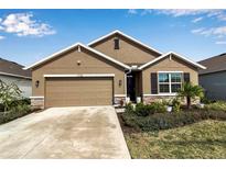 Tan house with brown garage door, landscaping, and a stone facade at 17741 Canopy Pl, Bradenton, FL 34211