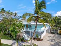 Beautiful light blue Key West home featuring a well-manicured lawn, lush tropical foliage, and a brick driveway at 3445 Anglin Dr, Sarasota, FL 34242