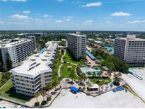 Aerial view of a beachfront community with multiple buildings, lush landscaping, and a pool at 5916 Midnight Pass Rd # 103, Sarasota, FL 34242