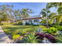 Beautifully landscaped front yard featuring tropical plants and a well-maintained lawn with a white house and red tile roof at 1864 Clematis St, Sarasota, FL 34239