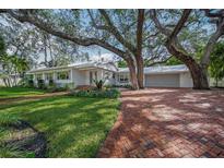 White single story home with brick driveway, lush landscaping, and large shade trees at 3331 Old Oak Dr, Sarasota, FL 34239