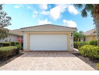 Two-car garage with a brick paver driveway and well-maintained landscaping at 6063 Benevento Dr, Sarasota, FL 34238