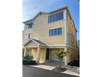 Three-story building with attached garage, featuring a light yellow exterior and a palm tree in the front at 611 Cedars Ct, Longboat Key, FL 34228