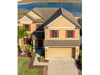 Two-story home with tan siding, red shutters, a well-manicured lawn and a 2 car garage at 14318 Fissore Blvd, Wimauma, FL 33598