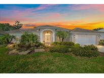 Charming home with a well-manicured lawn, lush tropical landscaping, and a colorful sunset sky at 2023 Micanopy Trl, Nokomis, FL 34275