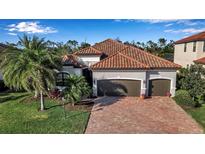 Beautiful home featuring a two-car garage, barrel tile roof and a brick paved drive framed by lush landscaping at 13303 Swiftwater Way, Lakewood Ranch, FL 34211