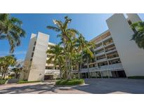 Low angle shot of a condominium building featuring palm trees, covered parking, and multi-level balconies under a clear, blue sky at 1932 Harbourside Dr # 244, Longboat Key, FL 34228