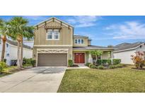 Two-story tan home featuring a landscaped yard, two-car garage, and a welcoming red double-door entrance at 5718 Westhaven Cv, Bradenton, FL 34203