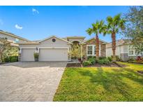 Charming single-story home featuring stone accents, three-car garage, lush lawn, and beautiful palm trees at 5821 Hevena Ct, Palmetto, FL 34221