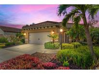 Charming home featuring a tile roof, two-car garage, and lush landscaping, illuminated by stylish outdoor lighting at 13106 Deep Blue Pl, Bradenton, FL 34211