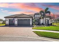 Beautiful single-story home featuring a three-car garage, tiled roof, and an attractive brick driveway with tropical landscaping at 20078 Elegante Ct, Venice, FL 34293