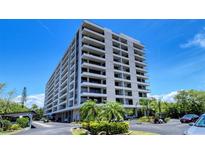 Multi-story condo building shows tropical landscaping and a parking area on a clear, sunny day at 6415 Midnight Pass Rd # 508, Sarasota, FL 34242