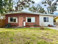 Charming, single-story brick home featuring a vibrant pink door, well-maintained lawn, and mature shade trees at 1520 2Nd E Ave, Bradenton, FL 34208