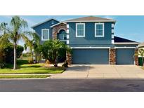 Two-story house featuring a blue exterior, stone accents, and a three-car garage at 2736 Suncoast Lakes Blvd, Punta Gorda, FL 33980