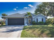 Gray house with dark garage door, landscaping, and a palm tree at 5255 Drew Rd, Venice, FL 34293