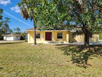 Charming single-story yellow home with a well-maintained front yard and a pop of color with its red front door at 12070 Surrey Ave, Port Charlotte, FL 33981