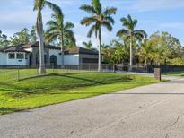 House exterior featuring a modern design, lush lawn, palm trees, and gated entrance at 5870 Hornbuckle Blvd, North Port, FL 34291