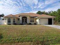 One-story home with a tan exterior, lush lawn, and a two-car garage at 1057 Staley St, Port Charlotte, FL 33952